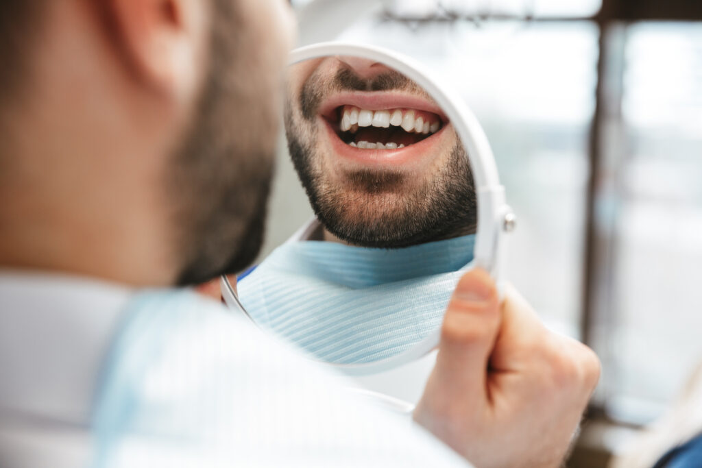 Man happily looking at his teeth in a hand mirror after getting dental filings